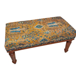 May include: A wooden footstool with turned legs and a top upholstered in a colorful patterned fabric. The fabric features a yellow background with blue and green floral and geometric designs.
