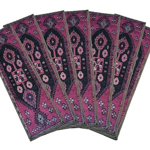 May include: A set of eight pink and black patterned fabric placemats with a geometric design. The placemats are arranged in a fan shape.