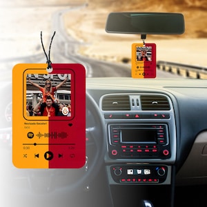 Peut inclure: Un diffuseur d'air de voiture jaune et rouge avec une photo de personnes lors d'un événement sportif. Le diffuseur d'air a un design de type Spotify avec le texte "Nevizada Geceleri 1905" et un bouton de lecture.