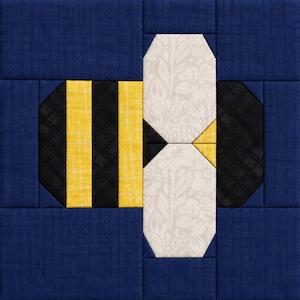 May include: A square fabric quilt block featuring a stylized bee design. The bee has a body made of alternating vertical yellow and black stripes, and wings crafted from light gray fabric with a subtle white floral pattern on a dark blue background.