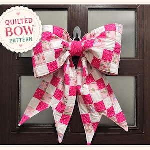 May include: A large, quilted bow in shades of pink and white, with a patchwork design. The bow is made of fabric squares and features a floral pattern. The text "Quilted Bow Pattern" is in a circular label.