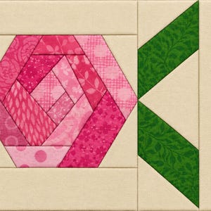 May include: A fabric quilt block featuring a central hexagonal rose motif constructed from various shades of pink patterned fabric. To the right of the rose are two green leaf shapes with a leafy print, all set against a solid cream background.