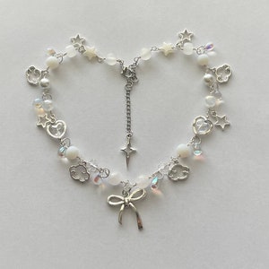 May include: A silver necklace with a bow charm, white beads, and silver charms in the shape of stars, hearts, and clouds.