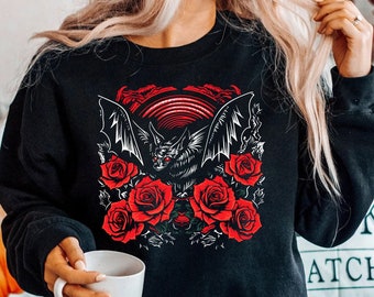 May include: Black sweatshirt with a graphic print of a bat with red roses. The bat is flying with its wings spread out. The roses are in bloom and have green leaves.