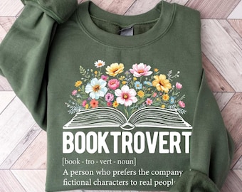 May include: Green sweatshirt with a white graphic of an open book with flowers on top. The text "BOOKTROVERT" is written below the book with the definition "[book - tro - vert - noun] A person who prefers the company of fictional characters to real people."