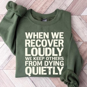 May include: A green sweatshirt with the text "When we recover loudly we keep others from dying quietly" printed in white.
