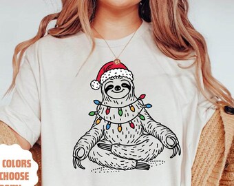 May include: A white t-shirt with a graphic of a sloth wearing a Santa hat and Christmas lights. The text '+10 colors to choose from!' is on the shirt.