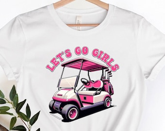 以下が含まれることがあります： ピンクのゴルフカートと「Let's Go Girls」というピンクの文字が書かれた白いTシャツです。