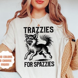Op de afbeelding: Een wit T-shirt met een zwart-witte illustratie van een chihuahua met de tekst "TRAZZIES FOR SPAZZIES" en " +10 COLORS TO CHOOSE FROM!"