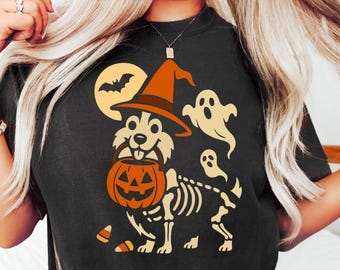 May include: Black t-shirt featuring a Halloween-themed graphic. The design includes a dog wearing a witch hat and carrying a jack-o'-lantern, with a skeleton body and ghosts. A full moon and bat are also included in the design.