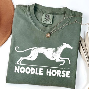 Może przedstawiać: Zielony T-shirt z białym siluetem charta i nadrukiem "NOODLE HORSE" z przodu.