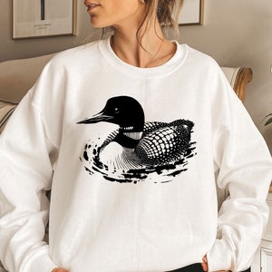 May include: White sweatshirt with a black and white graphic of a loon swimming in water.