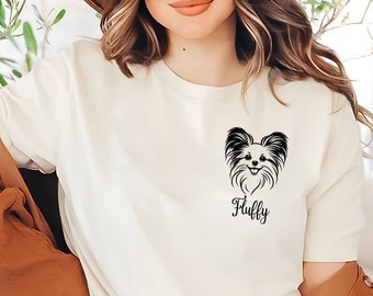 Puede incluir: Camiseta color crema con una ilustración en blanco y negro de un perro Papillon y la palabra "Fluffy" debajo. La camiseta está hecha de un material suave.