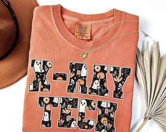 Puede incluir: Una camiseta naranja quemada con un gráfico negro que dice "X-RAY TECH" con fantasmas y calabazas en las letras.