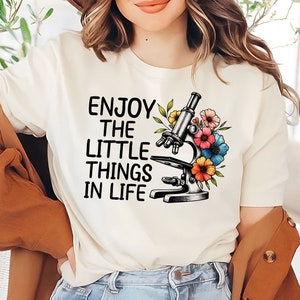 May include: White t-shirt with the text "Enjoy the little things in life" and a black and white illustration of a microscope with colorful flowers.