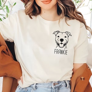 May include: A white t-shirt with a black line drawing of a pit bull dog and the name Frankie printed below the image.