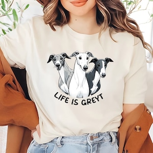 Può includere: Una maglietta bianca con una grafica di tre levrieri e il testo "Life is Greyt".