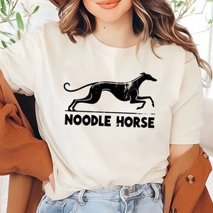 May include: White t-shirt with a black silhouette of a running greyhound and the text "NOODLE HORSE" printed on the front.