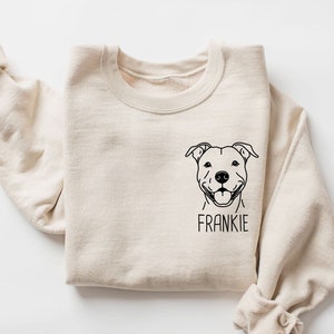May include: A beige sweatshirt with a black line drawing of a pit bull dog's face and the name "FRANKIE" printed below it.