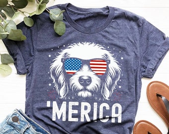 May include: A navy blue t-shirt with a white doodle of a dog wearing sunglasses with the American flag design. The text 'MERICA' is printed in white below the dog.