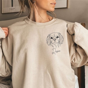 May include: A beige sweatshirt with a black line drawing of a dog's head and the name "Rosie" printed on the front.