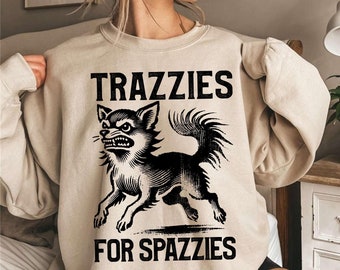 Può includere: Una felpa beige con una grafica nera di un chihuahua con il testo "TRAZZIES FOR SPAZZIES".