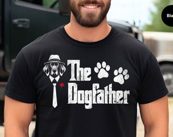 Può includere: Maglietta nera con una grafica bianca di un cane che indossa un fedora e una cravatta, con il testo "The Dogfather" e impronte di zampe.
