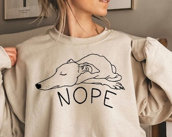 May include: A beige sweatshirt with a black outline of a dog lying down and the word "NOPE" printed on the front.