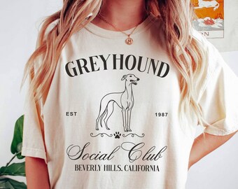 以下が含まれることがあります： グレーのTシャツに、グレイハウンドの犬、"Greyhound Social Club"の文字、"Est. 1987 Beverly Hills, California"の文字が黒で描かれたグラフィックデザインが施されています。