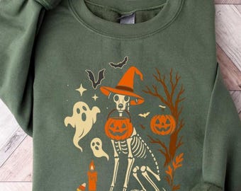 Puede incluir: Sudadera verde con un diseño de Halloween. El gráfico incluye un perro esqueleto con un sombrero de bruja y un cubo de calabaza. Otros elementos son fantasmas, murciélagos, una vela y una calabaza. El diseño es en naranja y blanco.