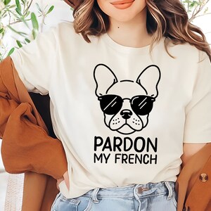 K&ouml;nnte beinhalten: Wei&szlig;es T-Shirt mit einer schwarz-wei&szlig;en Illustration eines franz&ouml;sischen Bulldoggen mit Sonnenbrille. Der Text "Pardon My French" ist unter dem Bild gedruckt.