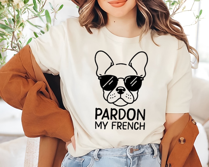 K&ouml;nnte beinhalten: Wei&szlig;es T-Shirt mit einer schwarz-wei&szlig;en Illustration eines franz&ouml;sischen Bulldoggen mit Sonnenbrille. Der Text "Pardon My French" ist unter dem Bild gedruckt.