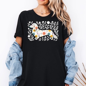 May include: Black t-shirt featuring a floral dachshund design. The dachshund is filled with colorful flowers and surrounded by white floral accents. The shirt has short sleeves and a relaxed fit.