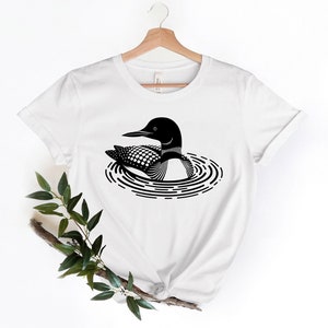 May include: White t-shirt with a black and white illustration of a loon swimming in a lake.