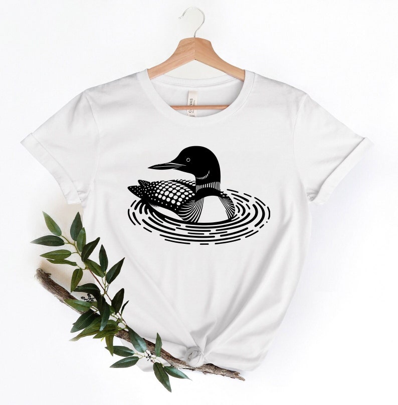 May include: White t-shirt with a black and white illustration of a loon swimming in a lake.