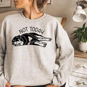May include: A light gray sweatshirt with the words "NOT TODAY" above a black and white graphic of a dog lying down. The dog graphic is detailed with black outlines and shading.