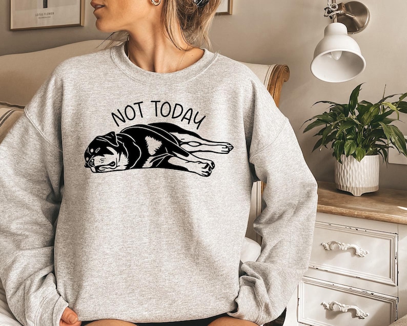 May include: A light gray sweatshirt with the words "NOT TODAY" above a black and white graphic of a dog lying down. The dog graphic is detailed with black outlines and shading.