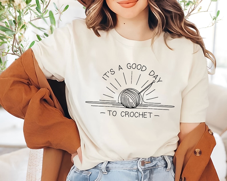 May include: A white t-shirt with a black graphic of a yarn ball and knitting needles with the text "It's a good day to crochet".