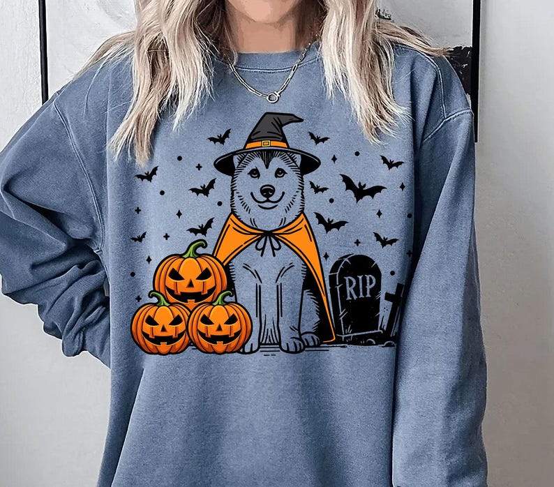May include: A blue sweatshirt with a graphic of a husky dog wearing a witch hat and holding pumpkins. The text "RIP" is on a tombstone in the image.