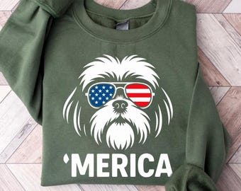 May include: An olive green sweatshirt with a white graphic of a dog wearing sunglasses in the style of the American flag. The word 'MERICA is printed below the dog graphic.
