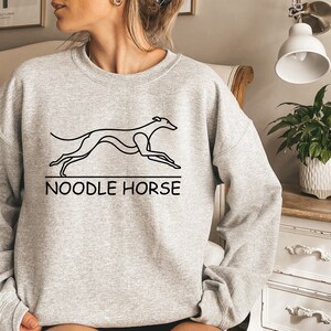 May include: A gray sweatshirt with a black line drawing of a running dog and the text "NOODLE HORSE" printed on the front.