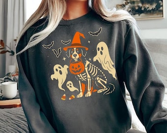 Puede incluir: Sudadera gris oscuro con un diseño de Halloween. El diseño incluye un perro con sombrero de bruja y una calabaza, con un contorno de esqueleto. También hay fantasmas y murciélagos.