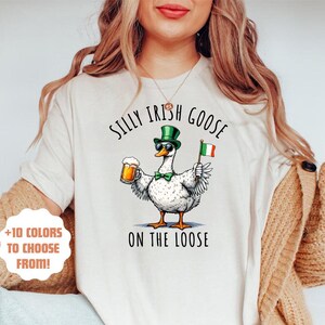 May include: White t-shirt featuring a green, white and orange goose wearing sunglasses and a green hat, holding a beer and an Irish flag. The text "Silly Irish Goose on the Loose" is printed on the shirt.