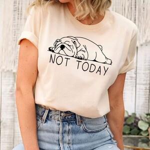 May include: A cream colored t-shirt with a black and white illustration of a bulldog sleeping and the text "NOT TODAY".