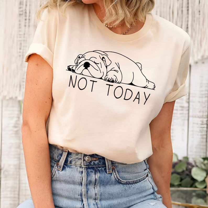 May include: A cream colored t-shirt with a black and white illustration of a bulldog sleeping and the text "NOT TODAY".