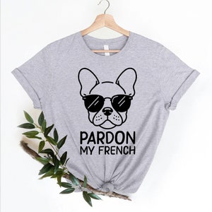 K&ouml;nnte beinhalten: Graues T-Shirt mit einer schwarz-wei&szlig;en Illustration eines franz&ouml;sischen Bulldoggen mit Sonnenbrille. Der Text "Pardon My French" ist unter dem Bild gedruckt.