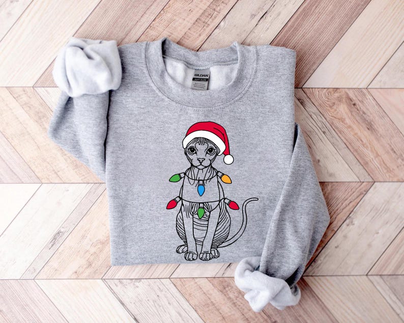 May include: A gray sweatshirt with a black and white illustration of a cat wearing a red Santa hat and Christmas lights.