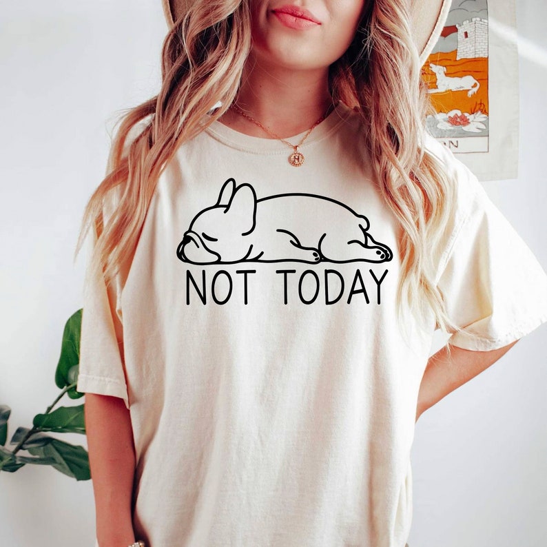 May include: A white t-shirt featuring a black outline of a sleeping French bulldog and the text "NOT TODAY".