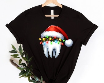 Op de afbeelding: Zwart T-shirt met een witte tand die een rode kerstmanmuts draagt en een string met kleurrijke kerstverlichting.