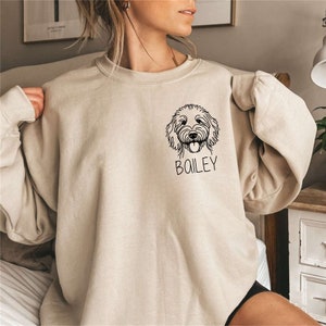 May include: A beige sweatshirt with a black line drawing of a dog's head and the name "Bailey" printed on the front.